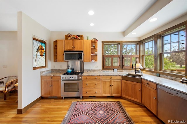 kitchen with open shelves, appliances with stainless steel finishes, light stone counters, a sink, and light wood-type flooring