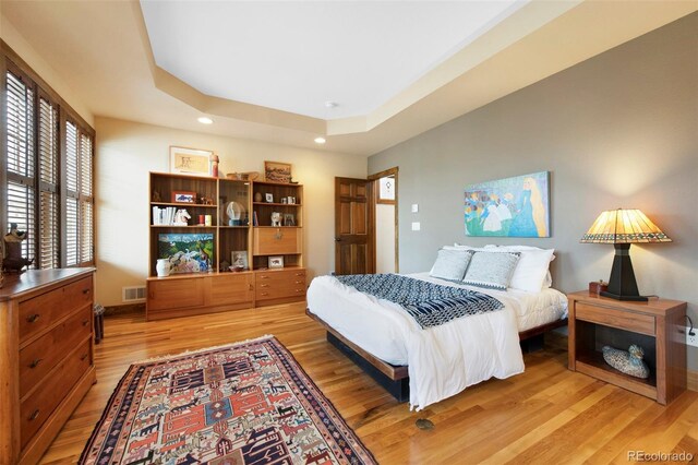 bedroom with a raised ceiling, light wood-style flooring, recessed lighting, baseboards, and visible vents
