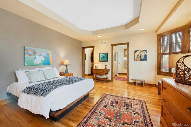 bedroom featuring visible vents, light wood-type flooring, baseboards, a raised ceiling, and recessed lighting