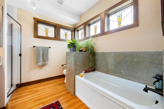 full bath with toilet, a shower stall, wood finished floors, visible vents, and a bath