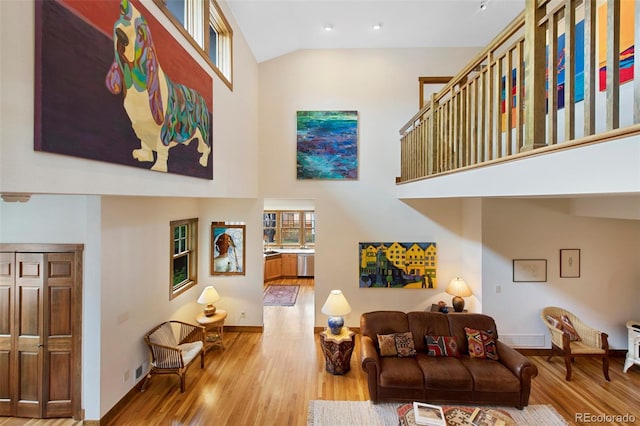 living area with baseboards, wood finished floors, and high vaulted ceiling