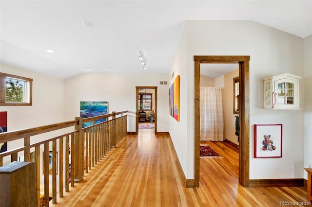 corridor with baseboards, light wood-style flooring, lofted ceiling, and visible vents