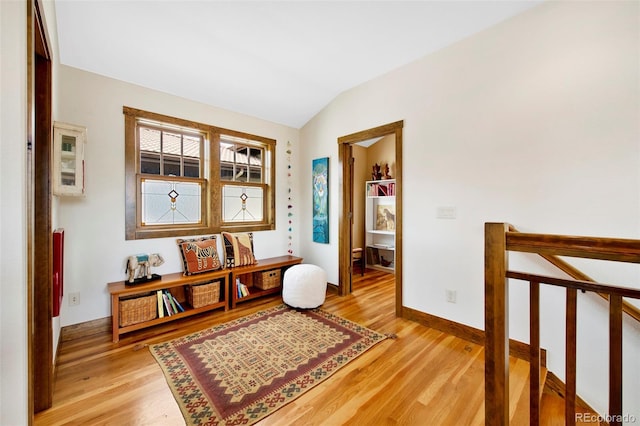 hallway featuring baseboards, vaulted ceiling, light wood finished floors, and an upstairs landing