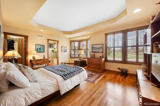 bedroom with a raised ceiling, recessed lighting, baseboards, light wood-type flooring, and visible vents