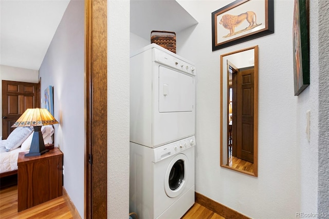 laundry room featuring baseboards, stacked washer / drying machine, wood finished floors, and laundry area