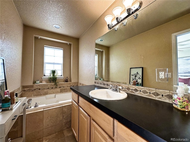 bathroom with vanity, a textured ceiling, and tiled bath