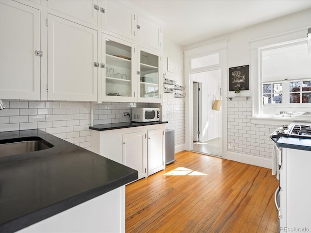 kitchen featuring white microwave, dark countertops, a sink, and white cabinetry