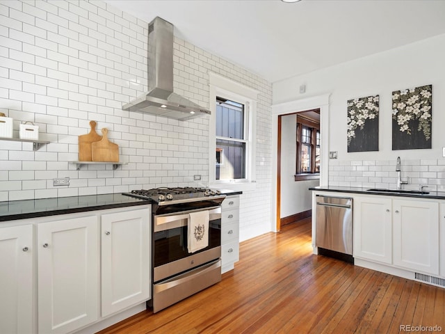 kitchen with wall chimney exhaust hood, appliances with stainless steel finishes, dark countertops, and a sink