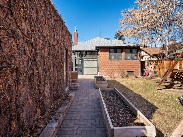 rear view of house with a shingled roof, a vegetable garden, a lawn, fence, and brick siding