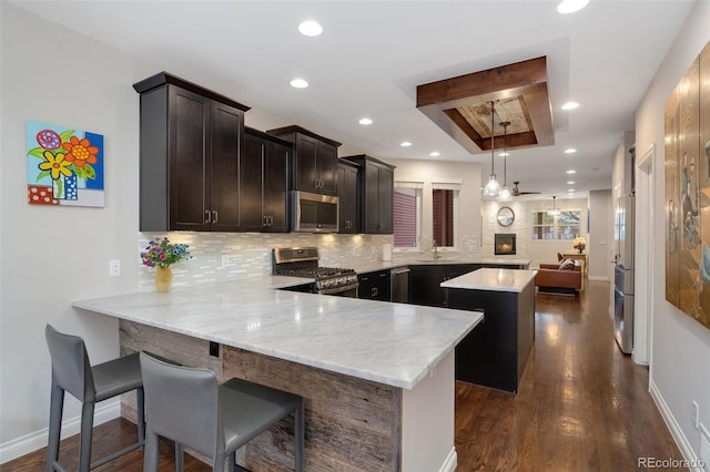 kitchen featuring decorative backsplash, a kitchen island, appliances with stainless steel finishes, a sink, and a peninsula