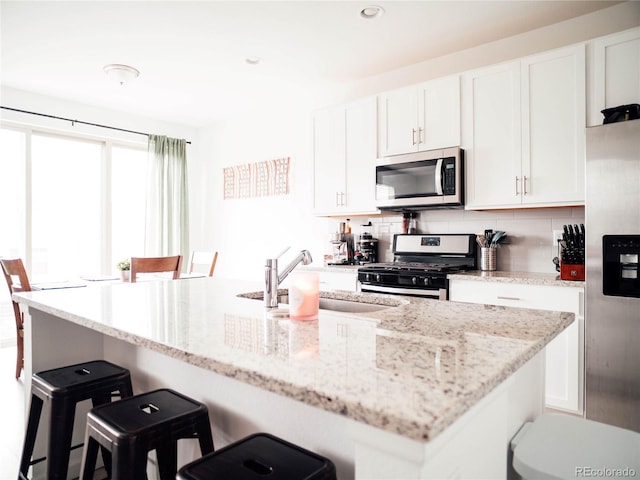 kitchen featuring white cabinets, appliances with stainless steel finishes, a sink, a breakfast bar area, and tasteful backsplash