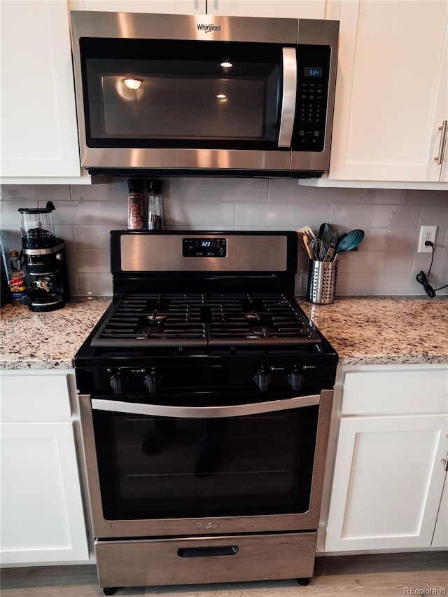 kitchen with white cabinets, appliances with stainless steel finishes, light stone counters, and tasteful backsplash