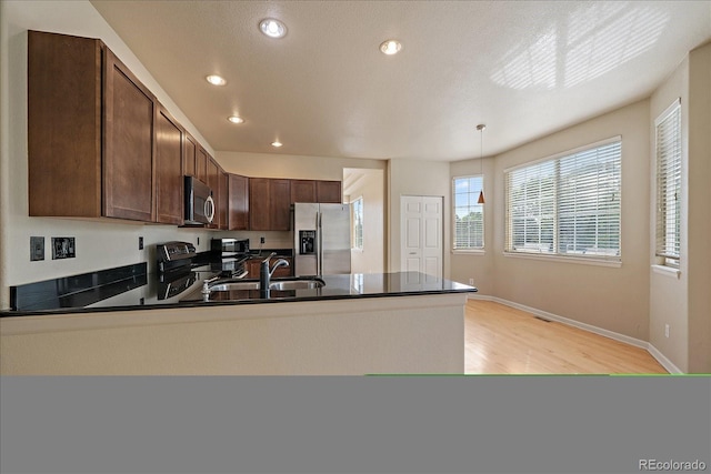 9602 Indian Wells Dr, Lone Tree, CO 80124 - kitchen with appliances with stainless steel finishes, dark countertops, a peninsula, a sink, and light wood-style flooring