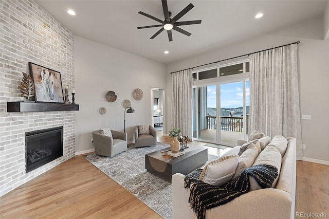 living room with light wood-type flooring, ceiling fan, and a fireplace