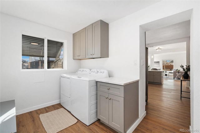 clothes washing area with cabinet space, washing machine and dryer, baseboards, and wood finished floors