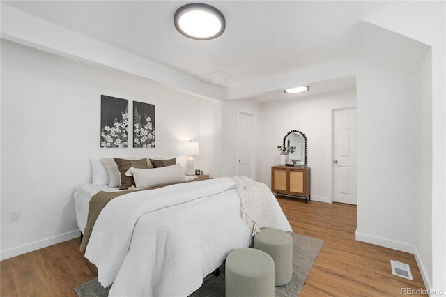 bedroom with baseboards, visible vents, and wood finished floors