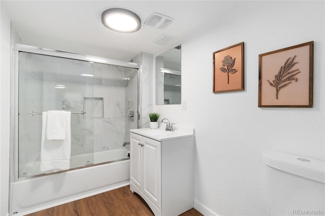 bathroom with visible vents, toilet, combined bath / shower with glass door, vanity, and wood finished floors