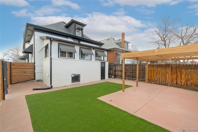 rear view of house with brick siding, a fenced backyard, a lawn, and a patio