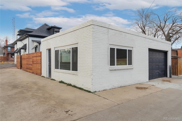 view of property exterior with a garage, driveway, brick siding, and fence