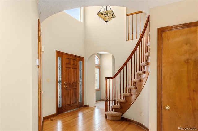 foyer with a towering ceiling, light wood-type flooring, arched walkways, and baseboards