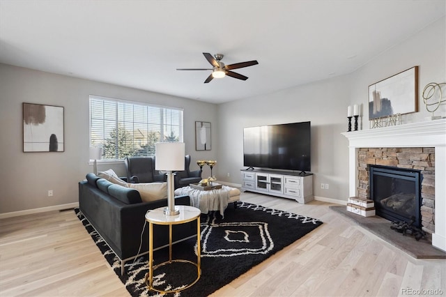 living room with a stone fireplace, ceiling fan, and light hardwood / wood-style flooring