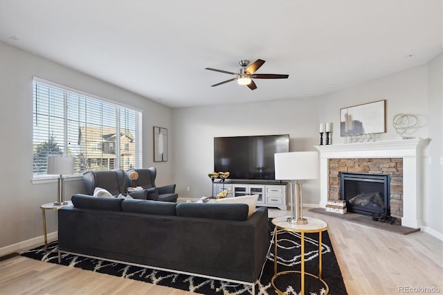 living room featuring ceiling fan, a stone fireplace, and light wood-type flooring