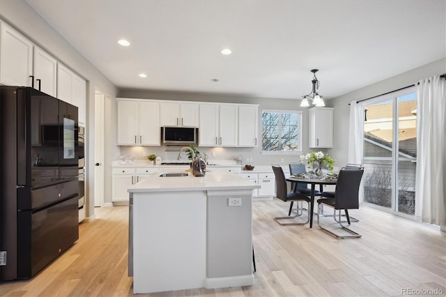 kitchen with sink, white cabinetry, pendant lighting, stainless steel appliances, and a kitchen island with sink