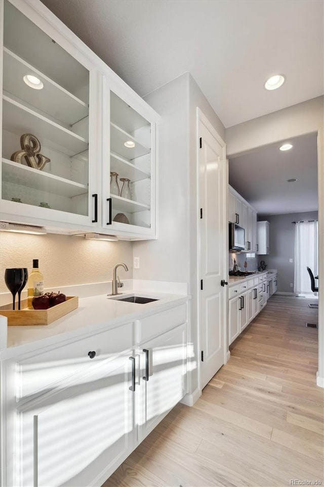 bar with light wood-type flooring, sink, and white cabinets