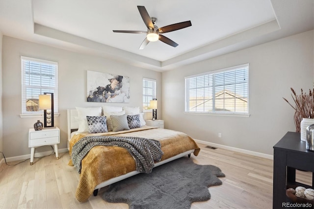 bedroom with ceiling fan, light wood-type flooring, and a tray ceiling