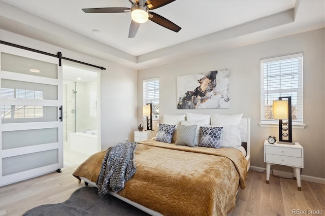 bedroom featuring ensuite bathroom, a barn door, a raised ceiling, and light hardwood / wood-style flooring