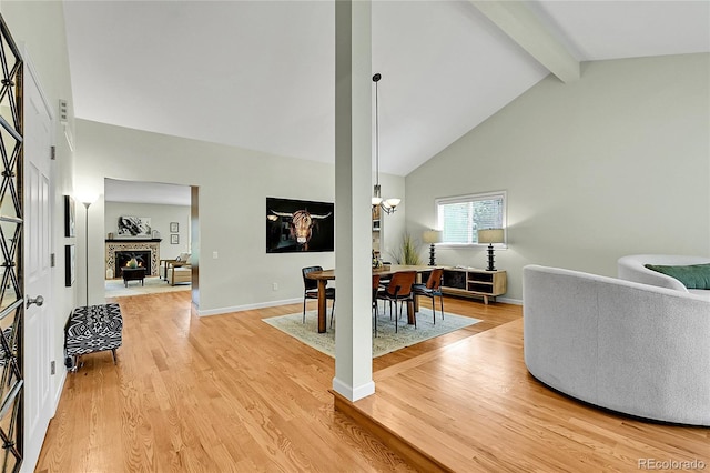 living area with beam ceiling, light wood-type flooring, a warm lit fireplace, a chandelier, and high vaulted ceiling
