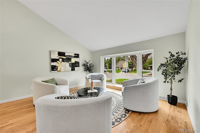 living area featuring baseboards, light wood-style floors, and lofted ceiling