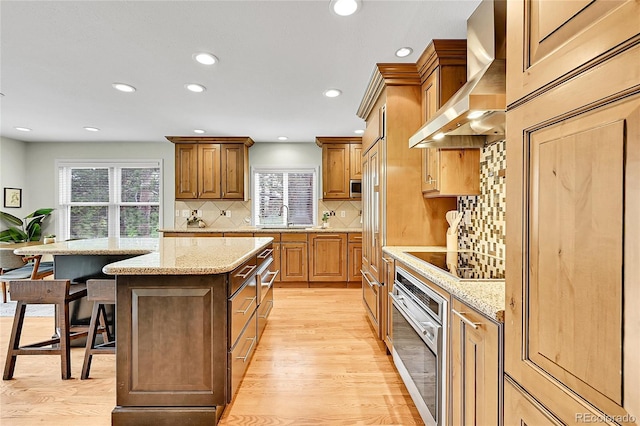 kitchen with appliances with stainless steel finishes, wall chimney exhaust hood, a kitchen island, decorative backsplash, and recessed lighting
