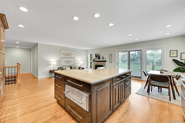 kitchen featuring light wood-style floors, a fireplace, recessed lighting, light stone counters, and a warming drawer