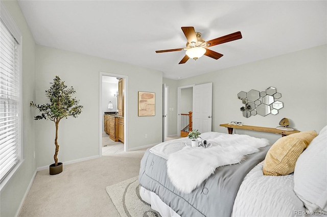 bedroom featuring light carpet, baseboards, ensuite bathroom, and ceiling fan