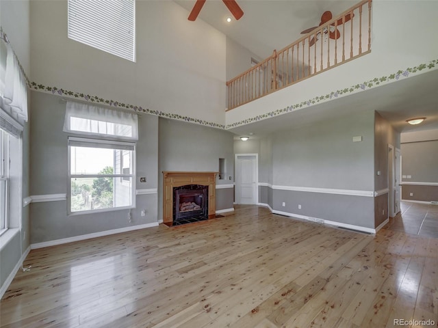 unfurnished living room featuring ceiling fan, a fireplace, hardwood / wood-style floors, and a towering ceiling