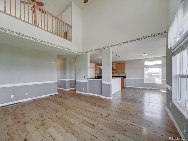 unfurnished living room featuring wood-type flooring, a towering ceiling, and ceiling fan