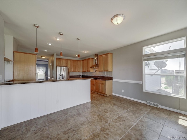 kitchen with decorative light fixtures, stainless steel fridge, backsplash, wall chimney range hood, and light brown cabinets