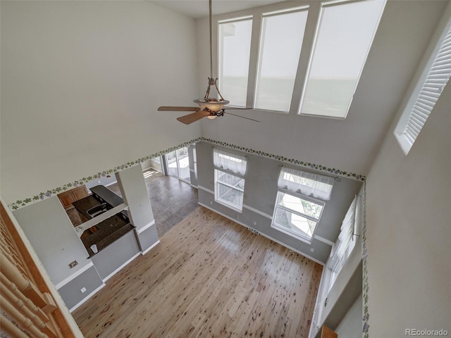 unfurnished living room featuring ceiling fan, a high ceiling, and light wood-type flooring