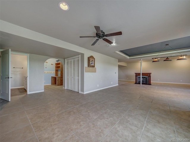 unfurnished living room featuring light tile patterned floors, ceiling fan, and a tray ceiling