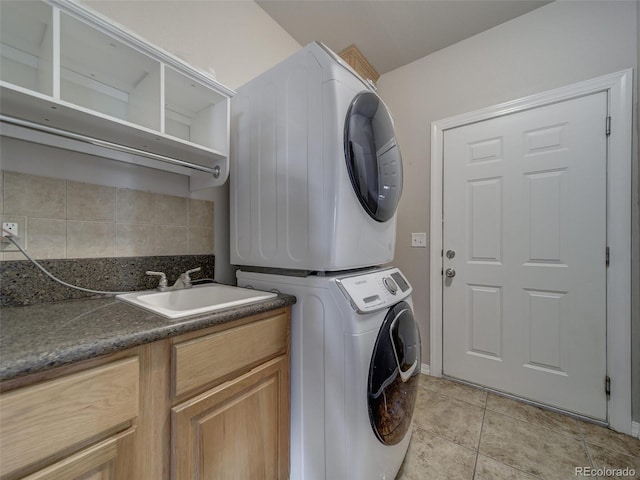 laundry room featuring cabinets, stacked washer and clothes dryer, sink, and light tile patterned floors