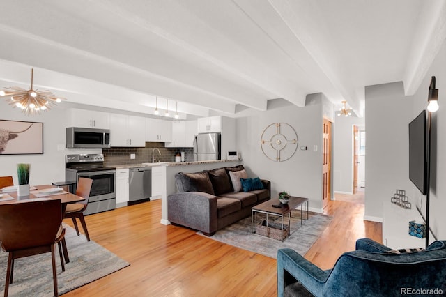 living room with an inviting chandelier, beam ceiling, and light wood-style floors