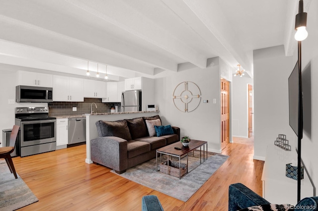 living area featuring beamed ceiling, baseboards, and light wood-type flooring