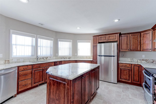 kitchen with light stone countertops, sink, a center island, and appliances with stainless steel finishes