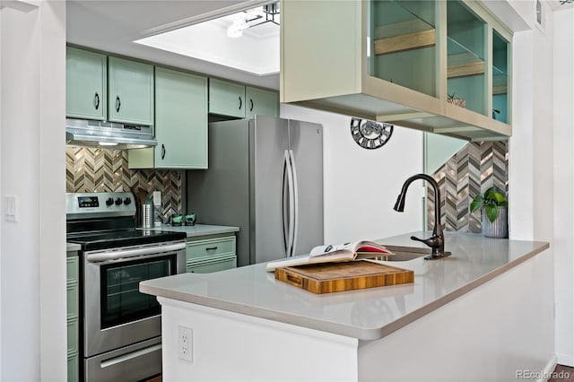 kitchen with tasteful backsplash, light countertops, under cabinet range hood, stainless steel appliances, and green cabinets