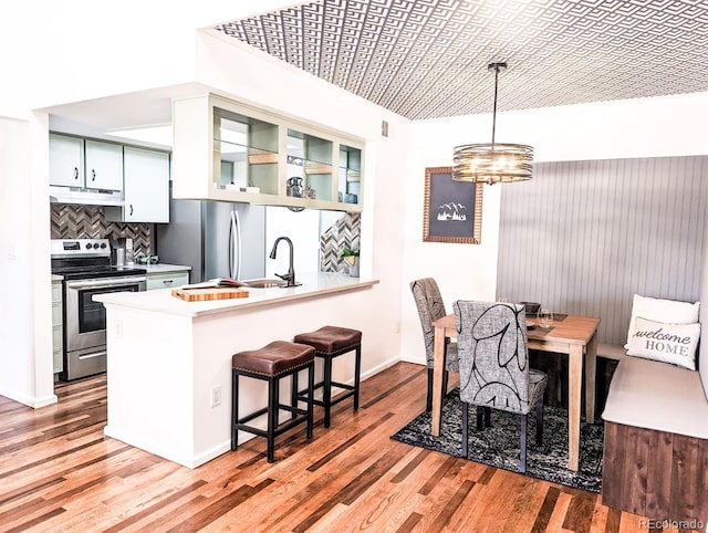 kitchen featuring light wood finished floors, stainless steel appliances, a peninsula, a sink, and under cabinet range hood