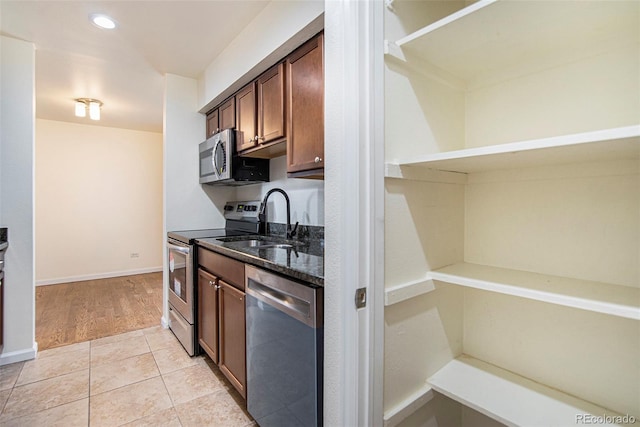 kitchen with stainless steel appliances, light wood-type flooring, sink, and dark stone counters