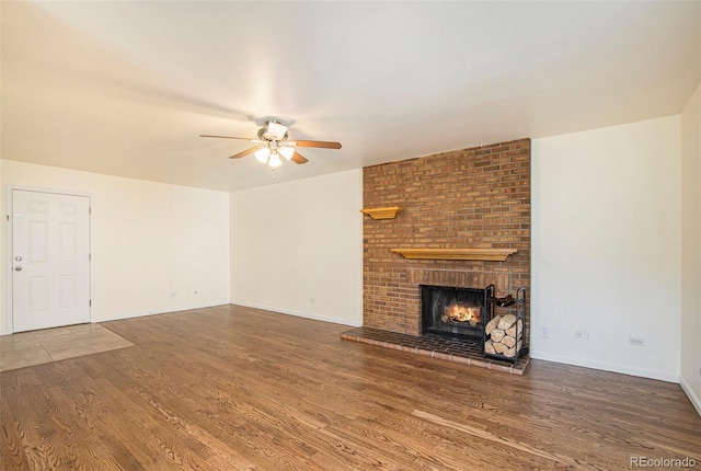 unfurnished living room featuring ceiling fan, a brick fireplace, and wood-type flooring