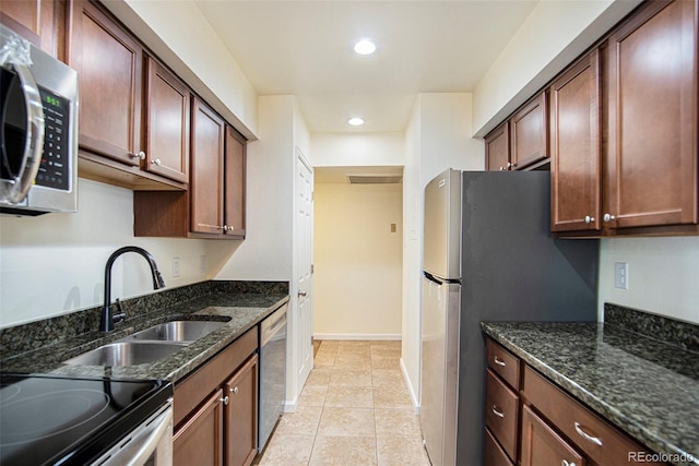 kitchen with sink, appliances with stainless steel finishes, light tile patterned floors, and dark stone counters