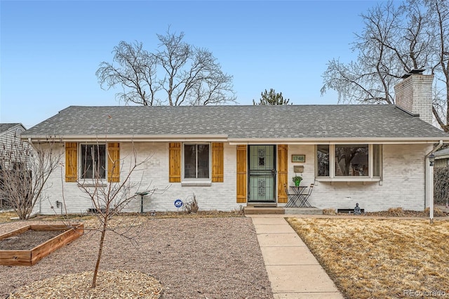 ranch-style home with a garden, a shingled roof, a chimney, and brick siding